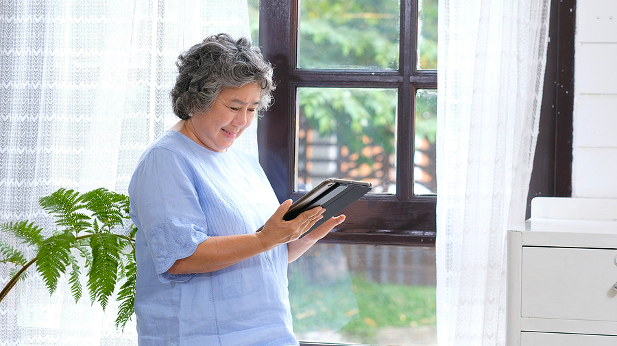 A person reading an e-newsletter on a tablet while using a communication device to assist with hearing loss.