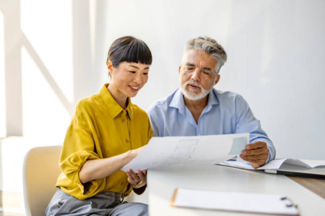 Two adults reviewing a floor plan at a table while planning home modifications for better hearing