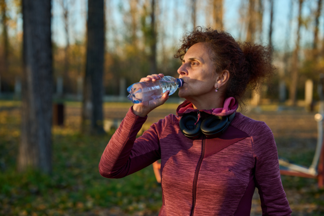 Older adult drinking bottled water on a wooded trail, staying hydrated on a cool fall afternoon