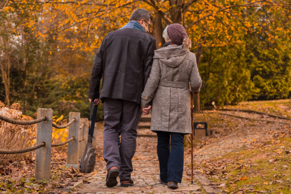 Two older adults, one using a cane, walking a leaf-covered path, a calm setting for mindfulness practices
