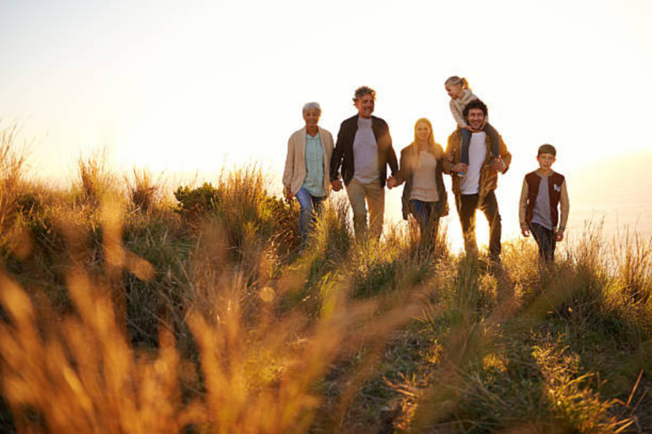 A family of three generations walking together through tall grass at sunset on a multi-generational trip