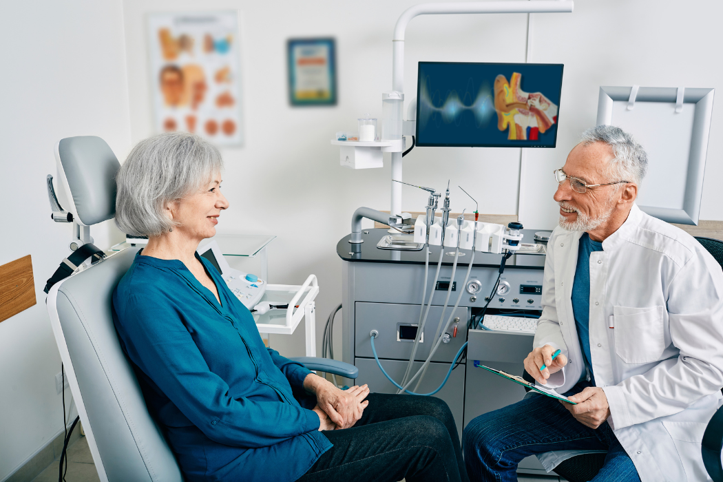 Older woman smiling as she talks with her audiologist during a hearing appointment in a bright exam room