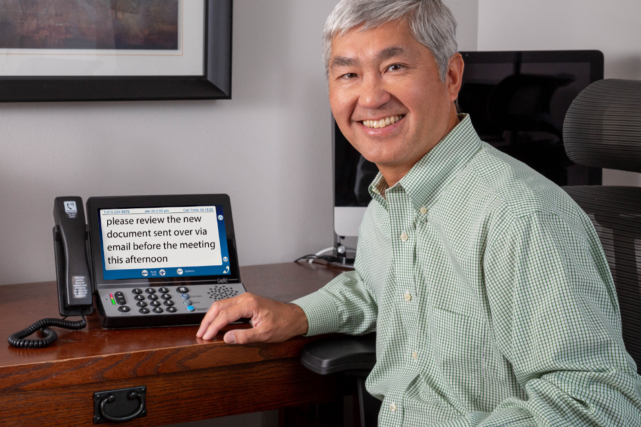 Man at a desk reading captions on a corded captioned phone, one option to weigh when choosing a corded or cordless phone
