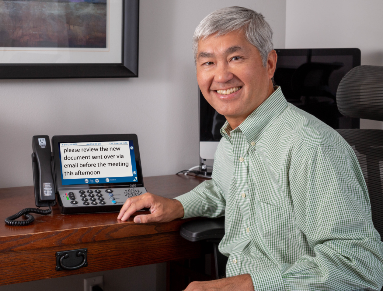 Man at a desk reading captions on a corded captioned phone, one option to weigh when choosing a corded or cordless phone